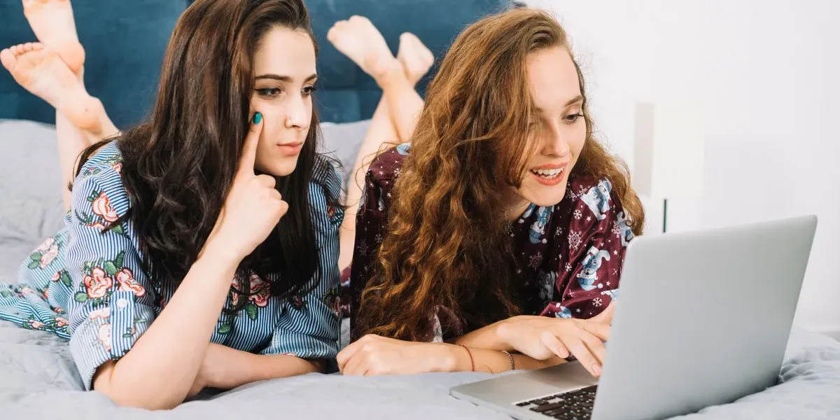 Young female friends lying on bed using laptop