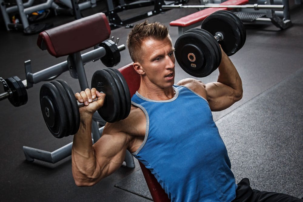 A man doing an incline dumbbell press in a gym